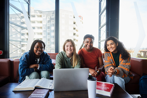 Portrait of a smiling group of diverse young female college students studying together in a student lounge between classes