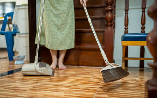 Low angle view of a young woman using a broom and dustpan to clean the floor of her apartment while doing housework at the weekend