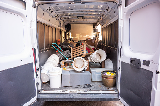 Back of cargo van, with back door open, full of objects such as buckets, pot, furniture, manual lawn mower.