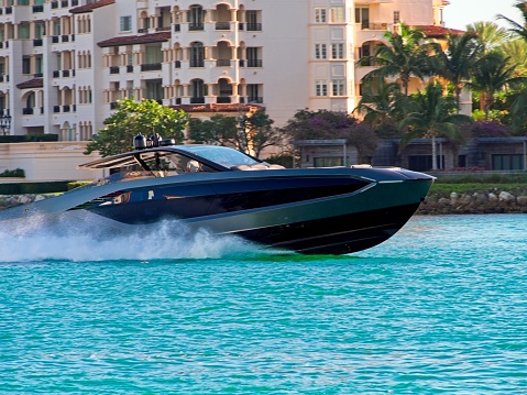 A high powered speedboat races through the turquoise hued channel waters into Miami harbor. The luxurious Fisher Island is in the background.