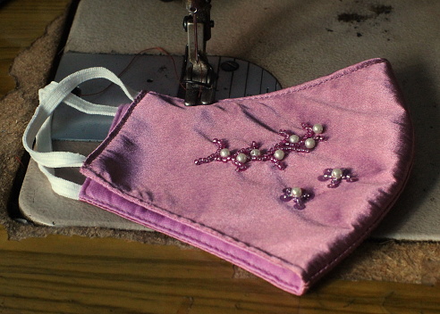 The process of sewing a simple pink cloth mask with beaded decoration.