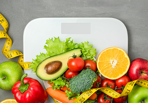 vegetables and fruits on scales on a gray concrete background. healthy eating and weight loss concept