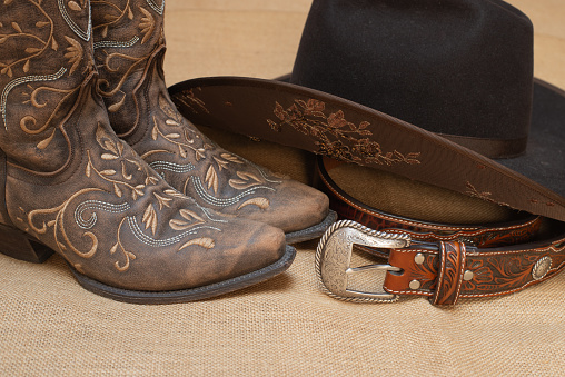 embroidered brown boots, dark brown hat and belt with silver buckle - text space on bottom - beige background - cowgirl style for country line dance