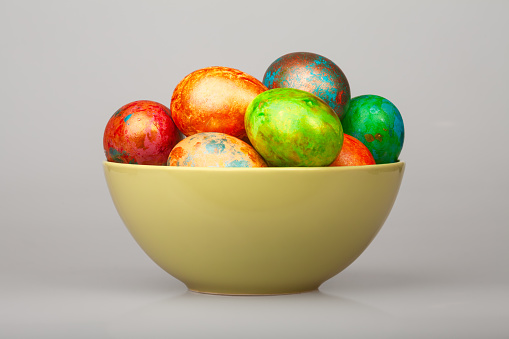 Colorful hand-painted easter eggs in a pastel ceramic bowl on grey background