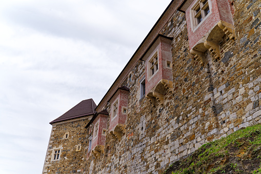 Looking up stone wall and tower with loophole of Ljubljana Castle on a cloudy summer day. Photo taken August 9th, 2023, Ljubljana, Slovenia.