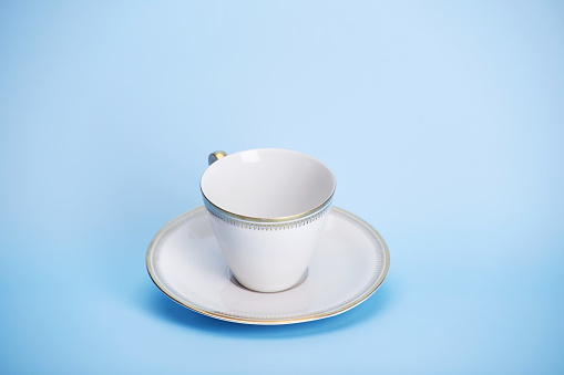 Tea coffee white cup bowl with golden pattern on the bright solid blue fond background