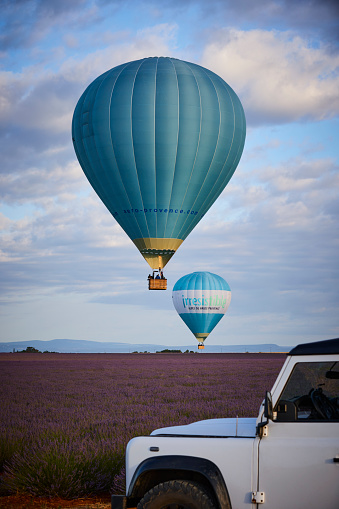 Land Rover 4x4 on the road next to a lavender field in Provence, France (Plateau de Valensole), two hot air balloons floating in the air on a beautiful morning in June