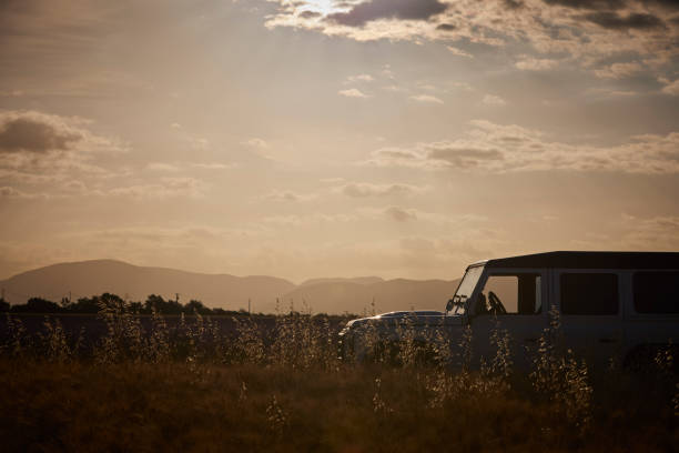 Land Rover 4x4 in a field with mountains in the back during sunrise.