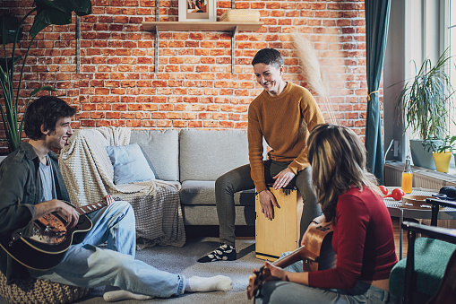 Three people, male and female musicians rehearsing their song in living room together.