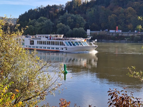 River cruise ship on Danube river near Passau city, Bavaria, Germany.White river boat with forest background at the autumn season.