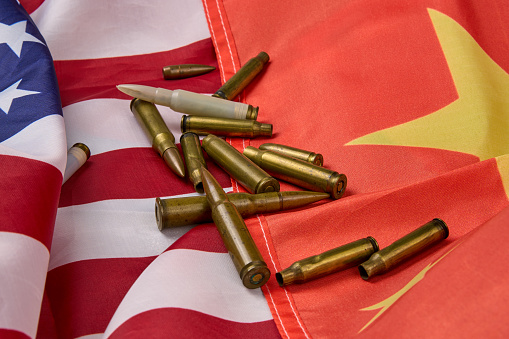 Close-up of cartridges and bullets of different sizes arranged on top of the American and Chinese flag.