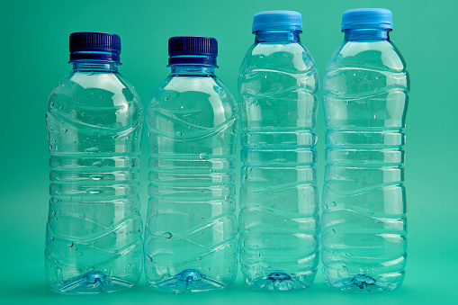 Closeup of open transparent plastic bottles of different shapes and sizes arranged in line against green background