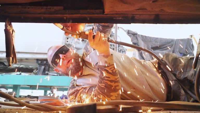 The mechanic uses a welding machine to repair a car threshold.