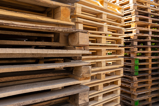 Piles of stacked natural wooden shipping pallets. Outside a big stack with big stack of wooden pallets.