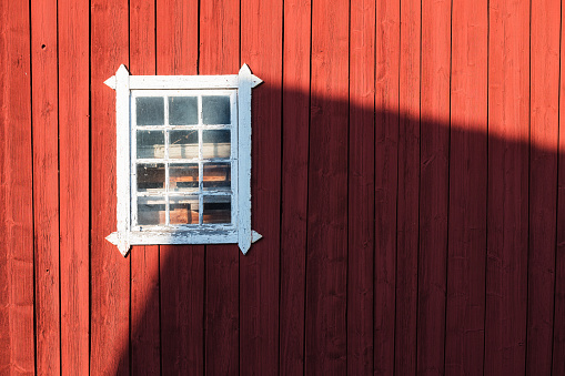 A red building in Sweden with a white window on its side, casting a shadow against the wall. The architectural details of the building and the contrast between the red and white elements create a striking visual.