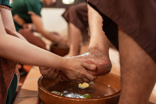 Close up of hands of masseur washing feet of woman customer in spa in bowl with water at spa salon.