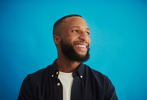 Portrait of a handsome young black man smiling while looking off to the side, shot a blue background. Stock photo