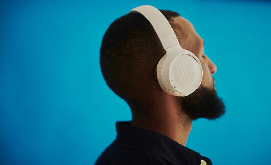 A young African man enjoying music with headphones, shot against a blue background