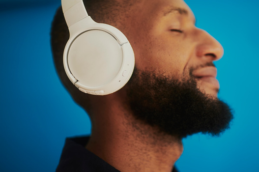 A young African man enjoying music with headphones, shot against a blue background