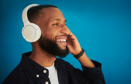 A young African man enjoying music with headphones, shot against a blue background with copy space. Stock photo