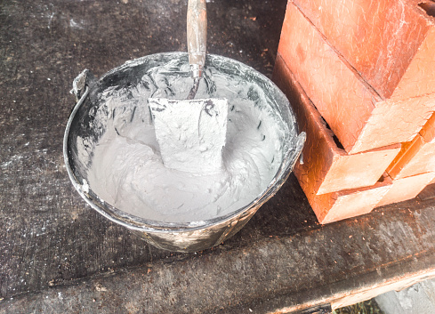 Bucket full white adhesive mortar ready for applicate. Bricks as background