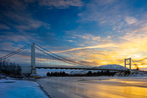Suspension Idubru bridge over Hvita River in winter with a sunset and blue sky