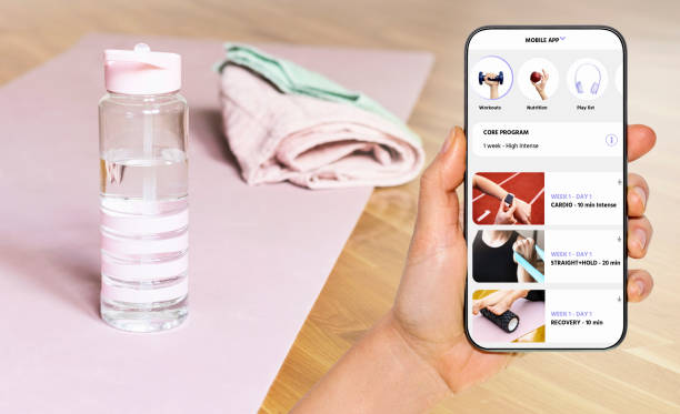 istock Home workout with sports mobile app. Sports mobile app interface on the phone screen in front of yoga mat, towel and bottle of water. 2048482587