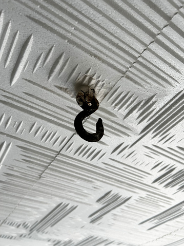 Empty old iron hook hanging on the ceiling background and ceiling with covering styrofoam