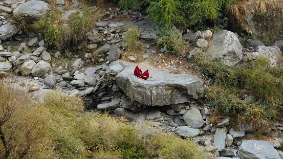 distant view of two monk sitting on rocks , Dhaaramshala, Himachal Pradesh, India- 28 Feb 2024