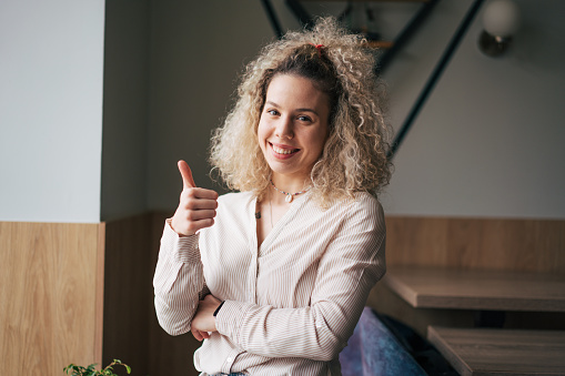 Portrait of beautiful young woman showing thumb up and smiling at camera.