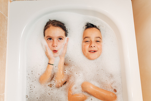 Above shot of children having fun with foam lying in a bathtub at home