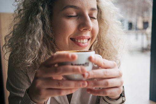 Headshot of young woman holding cup of coffee with eyes closed.