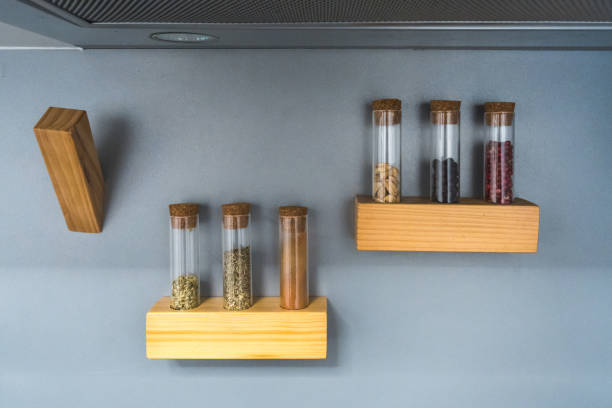A sleek, contemporary kitchen setup in a modern apartment, featuring wooden shelves with clear glass spice jars. The minimalist design emphasizes functionality and modern aesthetics, with spices organized neatly against a gray background.