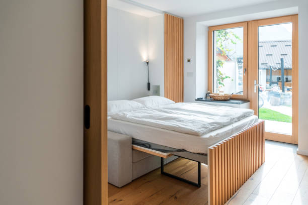 Bright and airy bedroom with a contemporary design in a modern apartment. Features a large bed with white linen, wooden headboard, and direct access to a patio. The room showcases a minimalist style with clean lines and a neutral color palette.