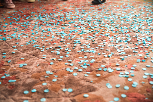 The floor is scattered with blue confetti indicating a baby boy's gender reveal. The festive event includes adults wearing casual footwear in an indoor setting, suggesting a private family gathering.