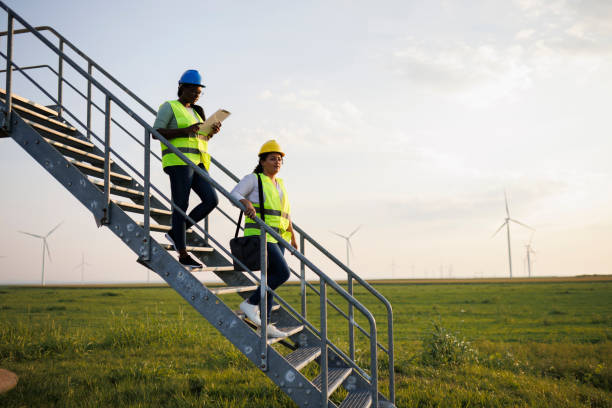 istock Two Female Engineer wearing uniform ,helmet hold document inspection work in wind turbine farms rotation to generate electricity energy 2048633739