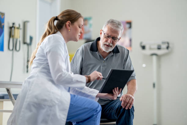 Senior Gentleman's Check-Up A senior gentleman meets with his female doctor to discuss his health concerns. He is dressed casually and seated in front of the doctor as she shares some recent test results with him on a tablet. patient stock pictures, royalty-free photos & images