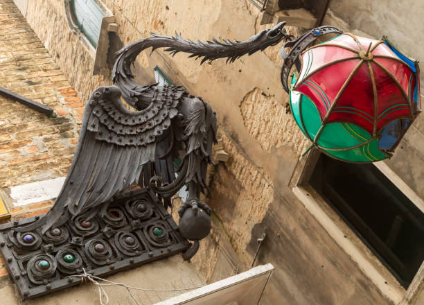 This is an image of an ornate metal dragon sculpture supporting a light formed out of three metal umbrellas. The umbrellas surround the light itself and are supported by a chain attached to the dragons mouth. The umbrellas are red, green and blue.