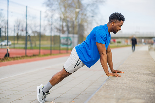 A young African American man captures the essence of vitality with his outdoor exercises, demonstrating that the pursuit of wellness knows no bounds, thriving beyond the confines of traditional gym walls