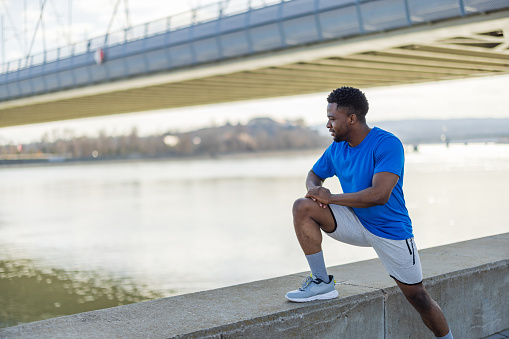 A young African American man choreographs his health routine within the city's framework, his outdoor exercises a dance with the environment, a creative expression of fitness and freedom