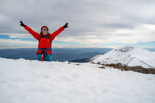 Alpinist climber is celebrating her success on snowy mountain crest on extreme harsh conditions with overcast sky before reaching the peak