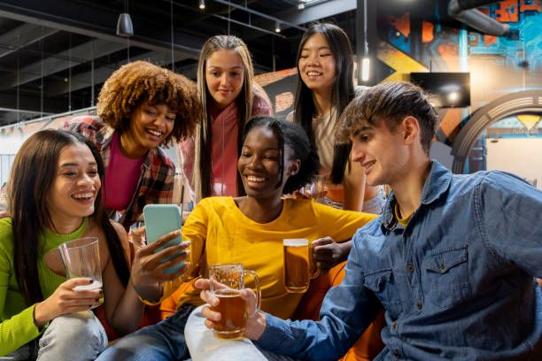 istock group of multicultural friends looking at mobile phone sharing gossip and talking while drinking sitting on sofa 2048718506