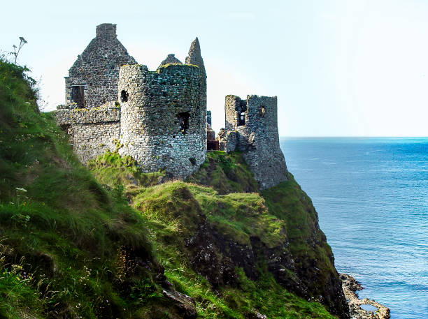 Dunluce Castle, County Antrim, Ireland, along the craggy coastline of Ireland, summer along the Antrim Coastal Route. Castle ruins on the coast of Ireland, with green hillsides, blue ocean, and cliff in the foreground.