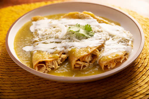 Green enchiladas. Typical Mexican dish made with a folded or rolled corn tortilla filled with shredded chicken and covered with spicy green sauce, cream, grated cheese and onion.