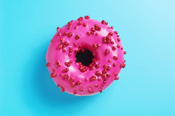 Pink donut with red sugar balls sprinkles on blue background, top view