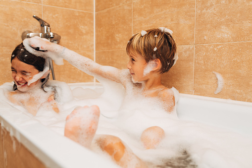 Siblings having fun splashing and playing in a bubble bath in the bathroom