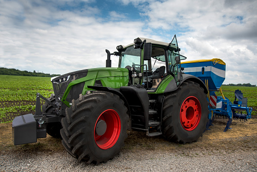 view of a new green tractor with a mechanical seeder near the field, planting a new crop of cereals