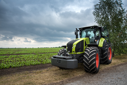 a new green tractor stands near the field, beautiful dramatic sky