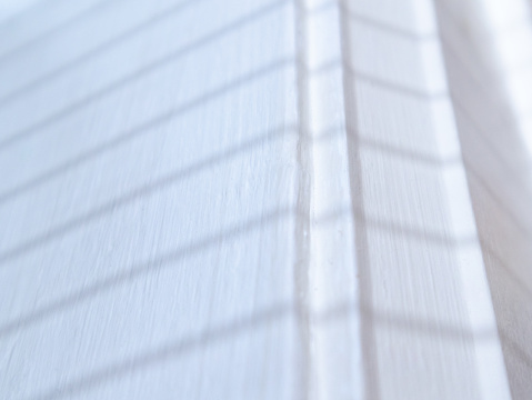 Close-up of shadow of window blinds on white painted molding. Abstract white background.