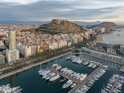 Capture the breathtaking beauty of Alicante from a unique perspective with this stunning early morning aerial drone photo. The image showcases the city center of Alicante, Spain, in the soft, golden light of dawn, offering a mesmerizing view of the coastal town and its surroundings.